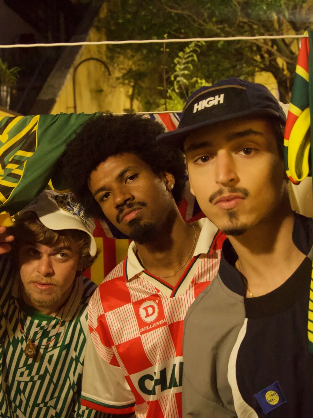 Integrantes da Milênio à noite, diante de bandeiras estendidas num varal.